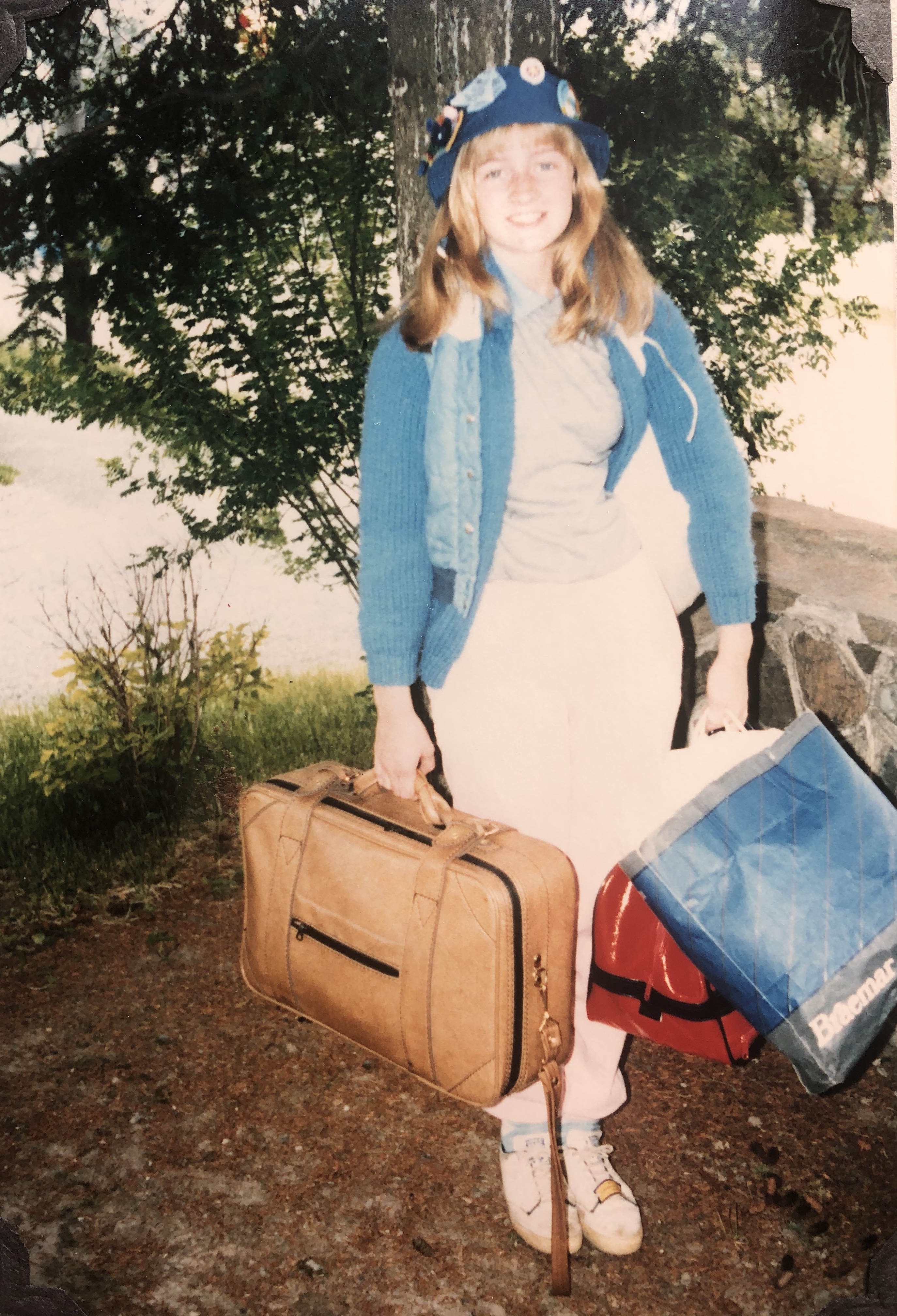Young teenager dressed for camping, standing outdoors, smiling and holding luggage
